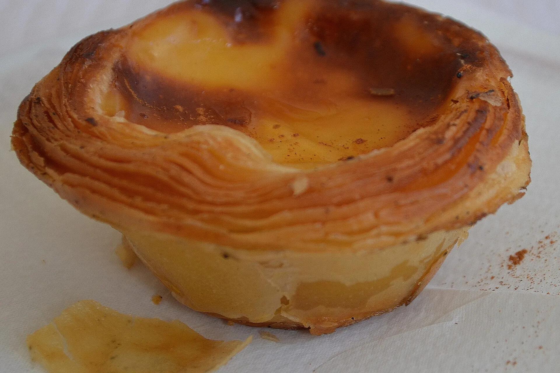 A Portuguese custard tart, a pastel de nata, with a blistered top and dusted with cinnamon